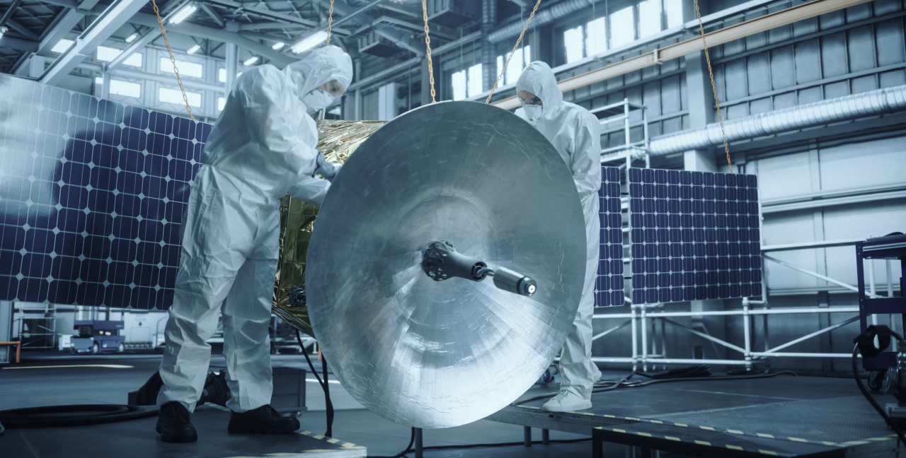 Technicians working on a satellite in a warehouse