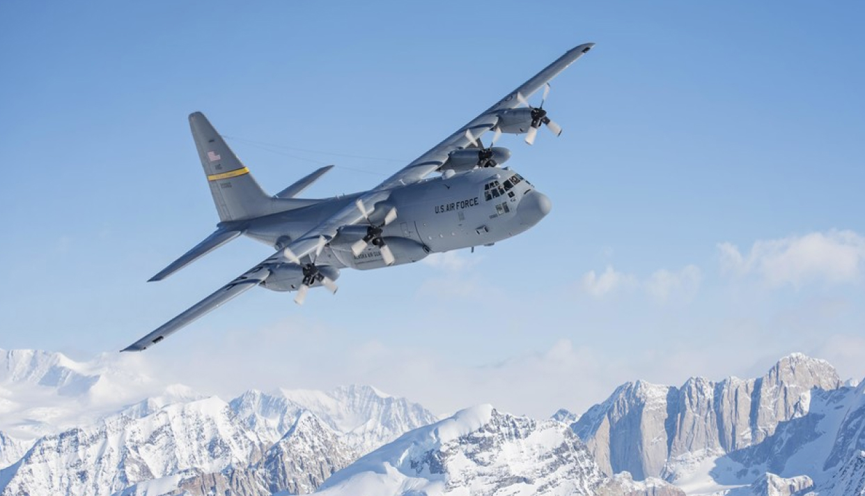 A C130 flying over snow-covered mountain tops.